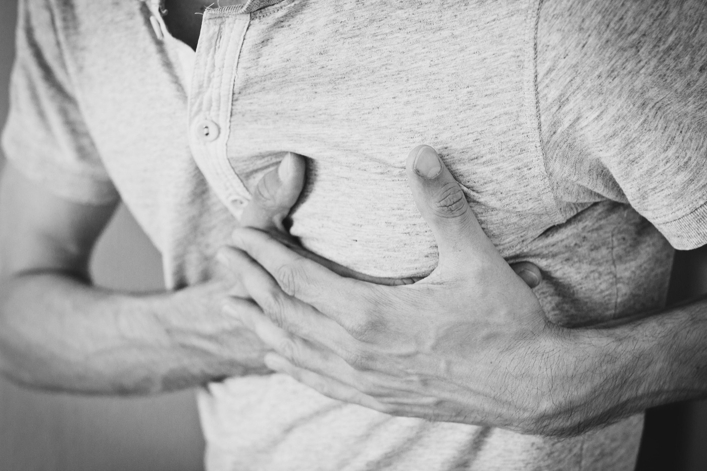 Black and white close-up of a person pressing both hands against their chest in pain