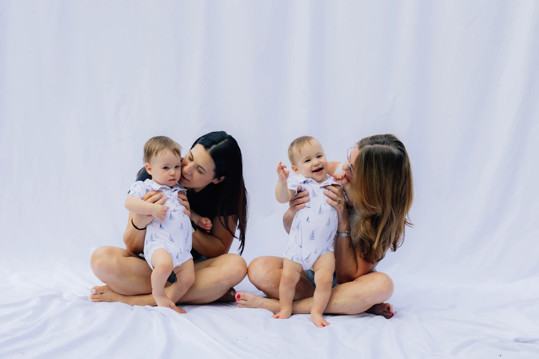 Two moms sitting together, each holding a smiling baby